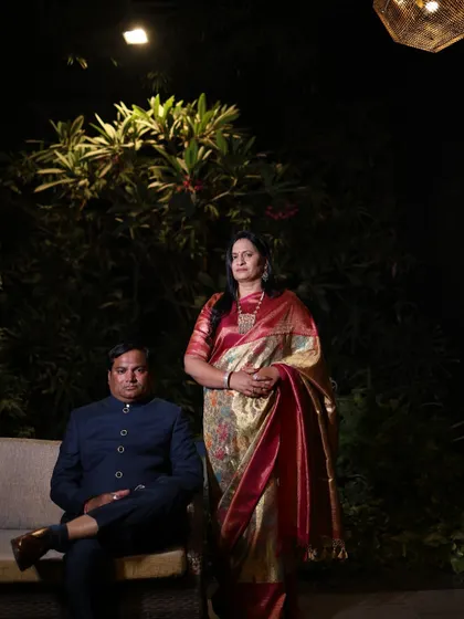 The parents of the groom posing for a formal portrait. The mother's ornate saree is perfectly balanced by the father's classic navy bandhgala, creating a portrait of sophistication.