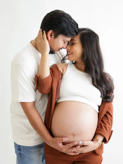 A modern and stylish couple's portrait. The mom-to-be's chic brown suit and exposed baby bump create a confident and contemporary look.