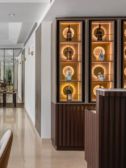 The bar area is a study in refined detail, featuring a fluted wooden counter and a stunning back-lit display with rotating shelves. This space is designed to be both a functional serving area and a decorative highlight.