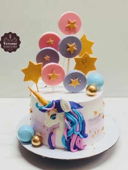 A unicorn-themed cake decorated with fondant lollipops and stars. The design features a beautifully molded unicorn on the side, with a mane made of blue and purple frosting.