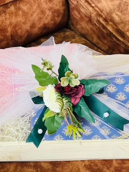 This wooden tray holds two elegantly wrapped gifts, showcasing how I handle clothing and other boxed items for a bridal trousseau. The floral arrangement on top adds a touch of sophistication.