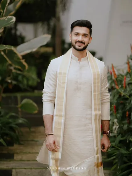 A handsome portrait of a groom in a traditional white kurta and mundu, ready for his South Indian wedding ceremony.