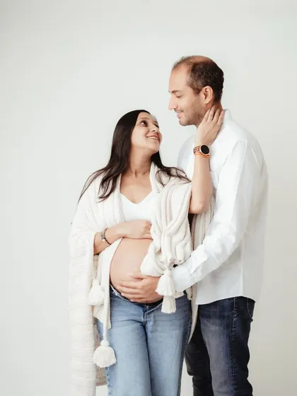A tender moment between an expecting couple. Dressed in casual whites and denim, their loving gaze shows the deep connection and excitement for their journey ahead.