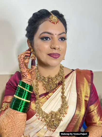 This bride's makeup features a beautiful matte finish with a deep berry lip, which works wonderfully with her off-white and maroon silk saree and temple jewelry.