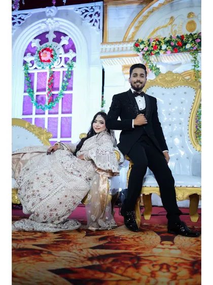 A regal portrait of the couple on their reception stage. The bride's elegant white and silver gown and soft makeup make her look like modern royalty.