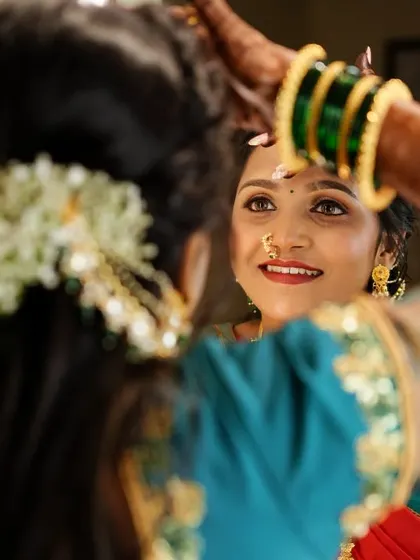 A bride's reflection, a moment of quiet contemplation before the ceremony. The mirror shot captures her smile as she adjusts her bindi, a classic getting-ready moment.