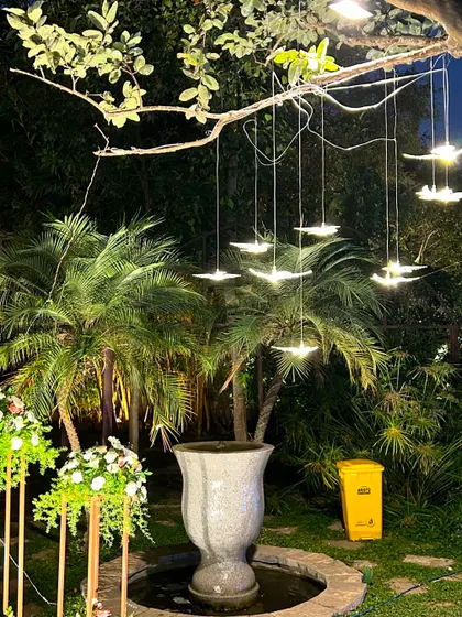 Modern, illuminated bird-shaped lights hang from tree branches, creating a magical and artistic lighting effect in the garden.