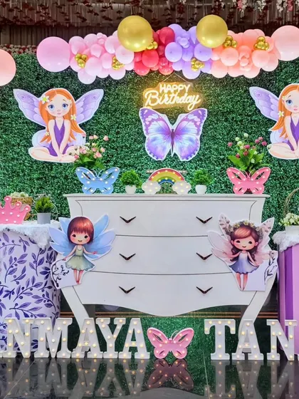 An enchanting fairy theme for twins Tanmaya and Tanay. The setup uses a unique white dresser as the centerpiece, surrounded by fairy and butterfly cutouts against a green hedge wall.