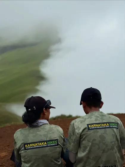 Two of our team members in Karnataka Hikes gear, looking out at the clouds rolling over the Netravathi ridge.