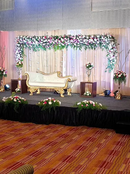 This is a classic floral arch stage design, perfect for a wedding celebration or reception. The arch is made of dense pink and white flowers over a simple white drape, with matching floral arrangements on either side.