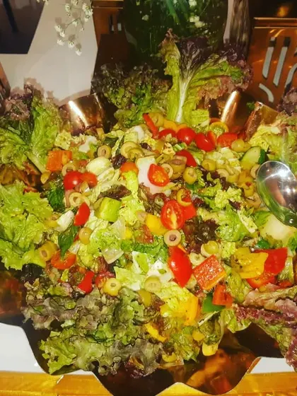 A mixed green salad with cherry tomatoes, olives, and bell peppers, served in a beautiful copper-toned bowl.