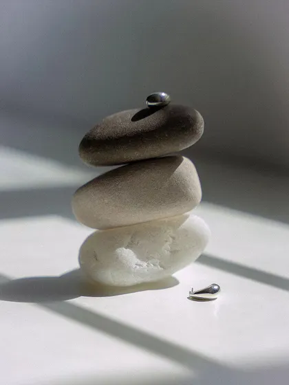 A minimalist still life composition for a jewelry shoot. The smooth, stacked stones and the play of natural light and shadow create a serene and balanced setting for the delicate silver earrings.
