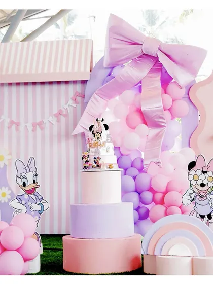 A grand Minnie and Daisy themed setup, featuring a large pink bow, character cutouts, and a multi-tiered cake, all in a lovely pastel color scheme.