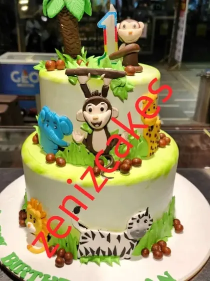 A fun, two-tier jungle animal theme cake. This design is covered in friendly fondant animals like monkeys, elephants, and zebras, making it a great choice for a young child's birthday.