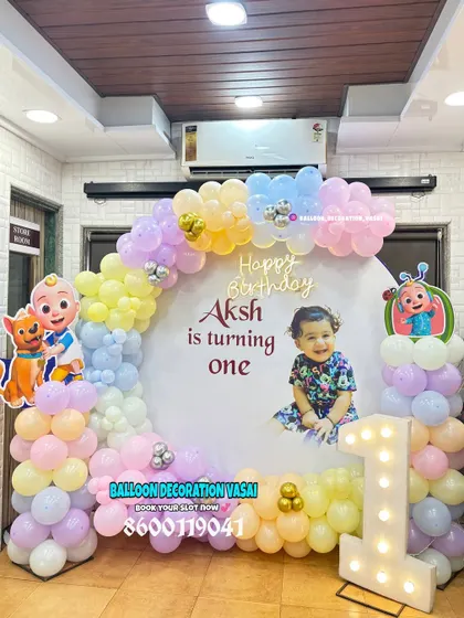 Aksh's Cocomelon-themed first birthday celebration. This home setup features a round backdrop with a custom photo, a pastel balloon arch, and Cocomelon character cutouts.