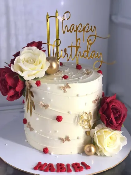 A glamorous birthday cake with red and white roses, gold butterflies, and the word "Habibi" for a loved one.
