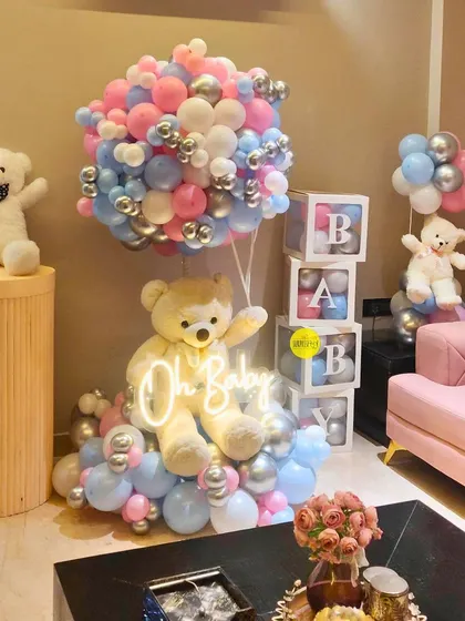 A cozy and cute teddy bear themed setup for an intimate baby shower. The "Oh Baby" neon sign on a large teddy, surrounded by pink and blue balloons, creates a perfect photo corner right in the living room.