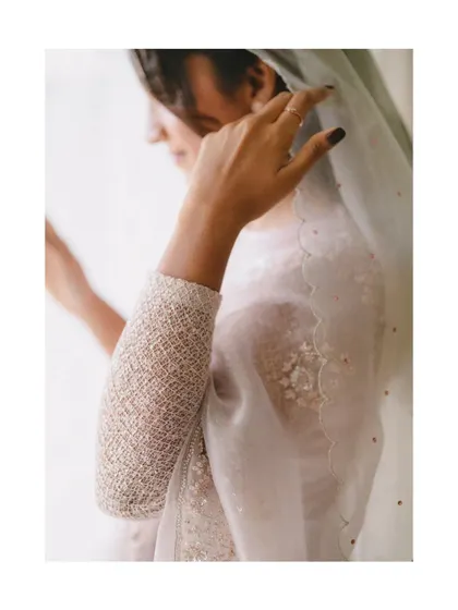 A close-up of the bride's hands as she adjusts her delicate, scalloped veil. This shot highlights the fine details of her attire and the grace in her movements.