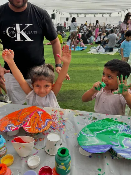 Two happy kids showing off their colorful hands and their finished fluid art pieces. This is what pure, uninhibited creativity looks like.