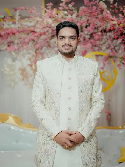 A classic portrait of the groom in his elegant off-white sherwani, standing before a backdrop of pink blossoms. His calm and happy expression sets the tone for the celebration.