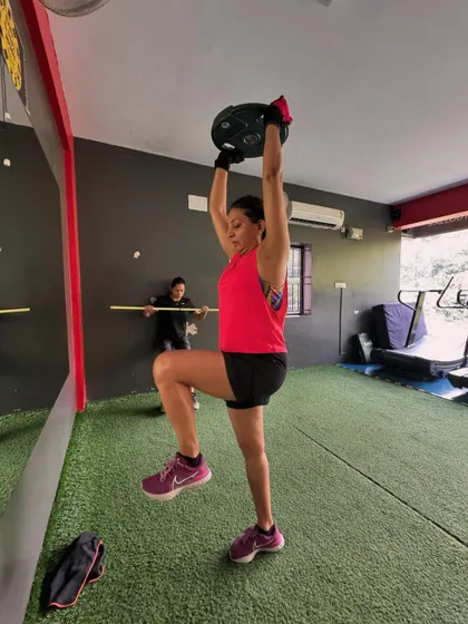 A client performs a single-leg step-up with an overhead plate press, a complex movement that challenges balance, strength, and coordination.