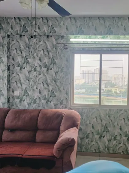 A living room with walls covered in a refreshing green and white leaf pattern. The wallpaper brightens the space and creates a natural, airy feel, even with a large sofa in front.