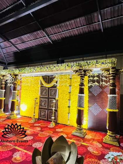 A majestic stage for a naming ceremony, featuring a wall of yellow flowers and large, ornate pillars. The design evokes the grandeur of a traditional temple entrance.