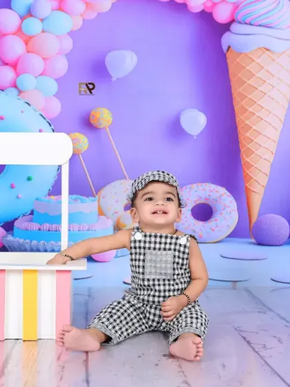 A baby boy sits in a sweet shop-themed setup, surrounded by giant donuts and ice cream cones. The pastel colors and fun props create a delicious and whimsical scene.