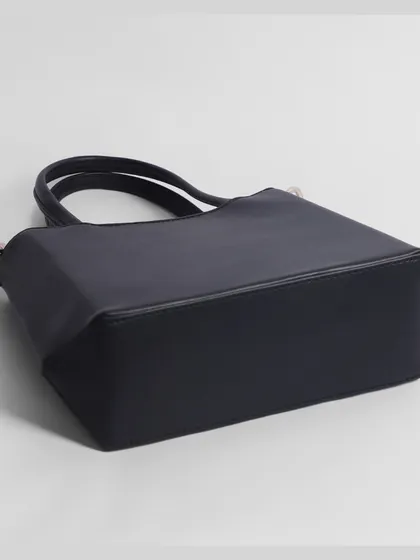 The base of a black handbag, photographed to show its shape and structure.