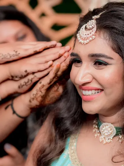 Fun and candid moments from a mehendi ceremony. The bride's makeup is fresh and playful, with a winged liner and glowing skin, perfect for celebrating with her loved ones. The hairstyle is a soft half-updo with pretty accessories.