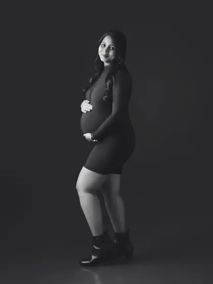 A full-length black and white portrait of a mom-to-be in a modern, form-fitting dress and boots.