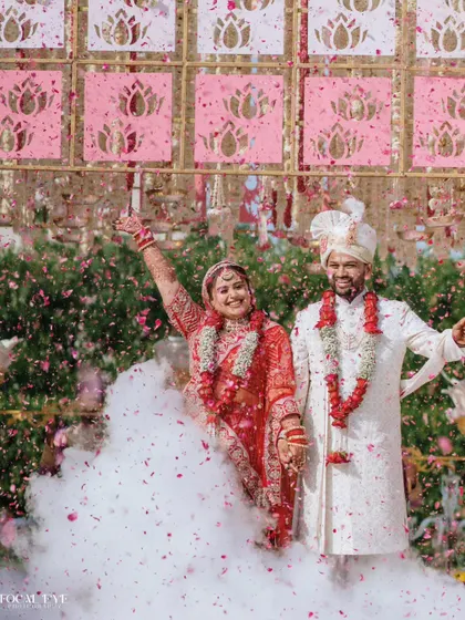 A moment of pure celebration for the bride and groom, surrounded by smoke and a shower of petals against a beautiful lotus-themed backdrop.