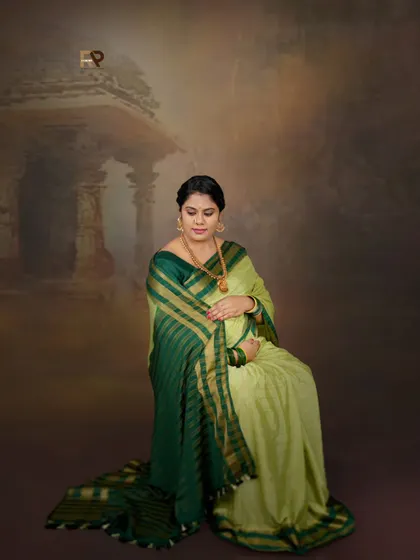 A quiet and contemplative portrait. The mom-to-be is seated in a two-tone green saree, with a backdrop depicting ancient temple ruins, creating a sense of peace and history.