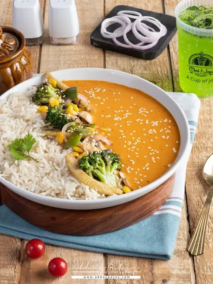 A Thai curry bowl shot with bright, appealing colors. The composition balances the main dish with a refreshing drink, presenting a complete and satisfying meal option for a menu.
