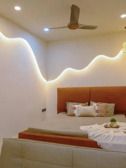 A minimalist bedroom from the 'Sukoon' project, featuring a platform bed and a unique wavy wall with integrated cove lighting for a dreamy effect.