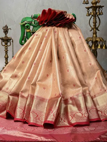 A beautiful peach-toned Kanjivaram silk saree with small red butis and a rich red and gold border. This is a classic bridal color combination, exuding warmth and grace.