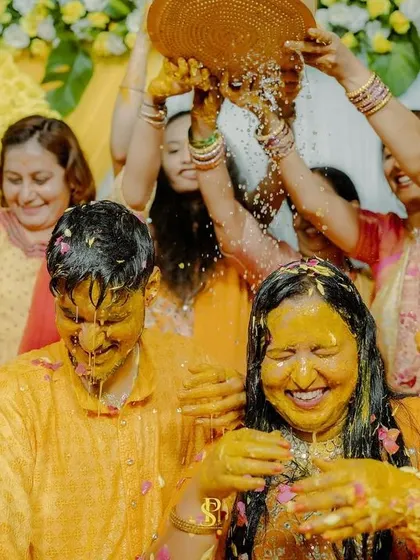 The couple sharing a laugh as they get completely covered in turmeric and water. This image is a testament to the fun, messy, and memorable nature of the Haldi.