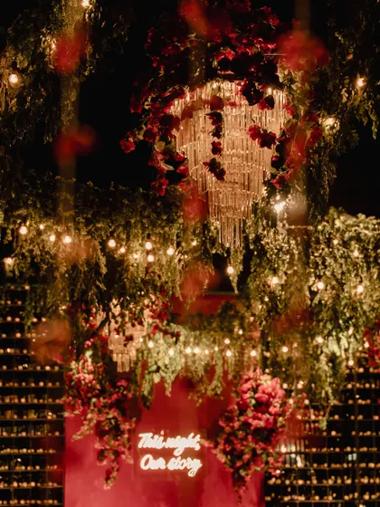 A view of the sangeet decor, showing how we layered elements to create depth. Cascading greenery, crystal chandeliers wrapped in red roses, and a backdrop of countless candles worked together to create a multi-dimensional, magical space.