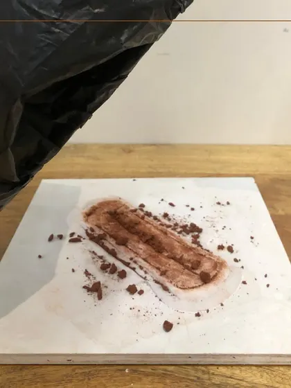 This piece directly confronts the stigma of menstruation. A sanitary napkin, 'soiled' with earth, is hidden under a black plastic bag, referencing the shame and secrecy often associated with a natural process.