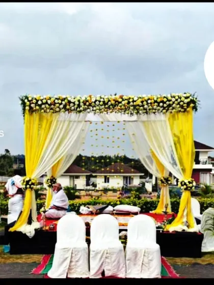 For outdoor ceremonies, I design beautiful mandaps that complement the natural surroundings. This setup uses bright yellow drapes and white floral arrangements to create a cheerful and elegant space for a daytime wedding.