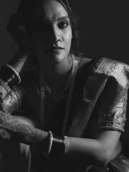 A dramatic, low-key black and white portrait. The use of shadow and light creates a moody, artistic feel, highlighting the bride's features and traditional attire in a unique way.