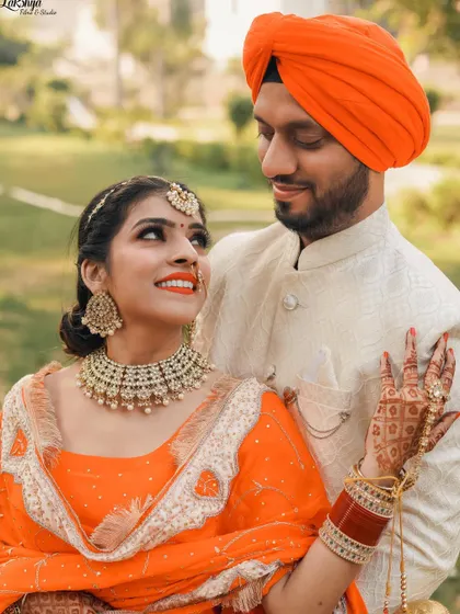 A classic romantic portrait where the bride is looking up at her partner. The bright orange of their traditional Punjabi outfits looks stunning in the natural light.