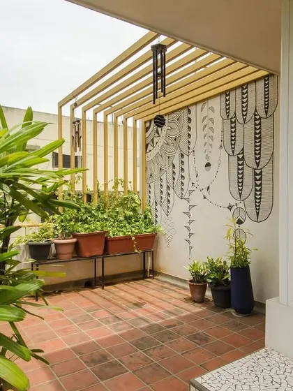 A black and white graphic mural provides a striking contrast to the vibrant plants on this terrace. A simple metal pergola adds structure and defines the space, creating a cozy and artistic outdoor nook.