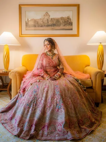 A picture-perfect moment for the bride, Shikha. Seated elegantly, her radiant makeup and stunning pastel lehenga come together to fulfill her bridal dreams.