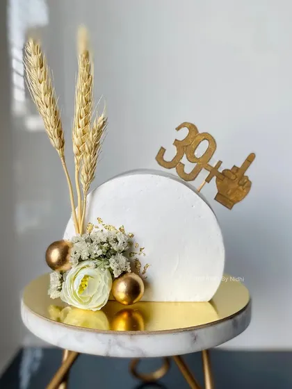A modern and minimalist cake-top-forward design for a 40th birthday. The clean white disc is accented with dried wheat, a white rose, and a cheeky topper.