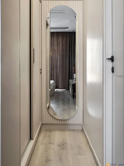 A view down the hallway of the master suite, showing the walk-in wardrobe with a full-length mirror. The light wood laminate flooring creates a clean and continuous look.