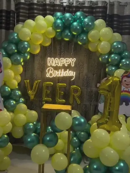 A Cocomelon themed first birthday with a circular balloon arch in green and yellow. This setup uses a custom backdrop, a neon sign, and a gold foil number '1' balloon.