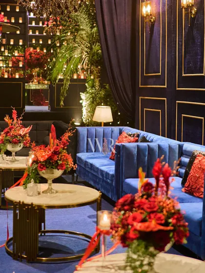 Another view of the blue velvet lounge, showing how we layer textures and lighting. A soft lamp, a wall of candles in the background, and rich floral arrangements create a warm and inviting corner.