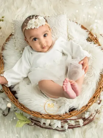 A sweet baby girl in a white lace outfit, showing off her cute little feet while sitting in a basket.