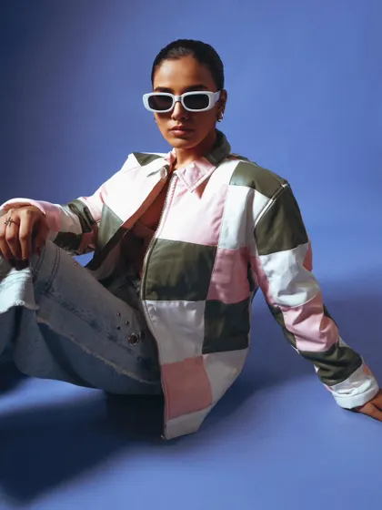 A relaxed, seated pose for a fashion lookbook. The patchwork jacket is the centerpiece, shot with clean lighting to show its colors and details.